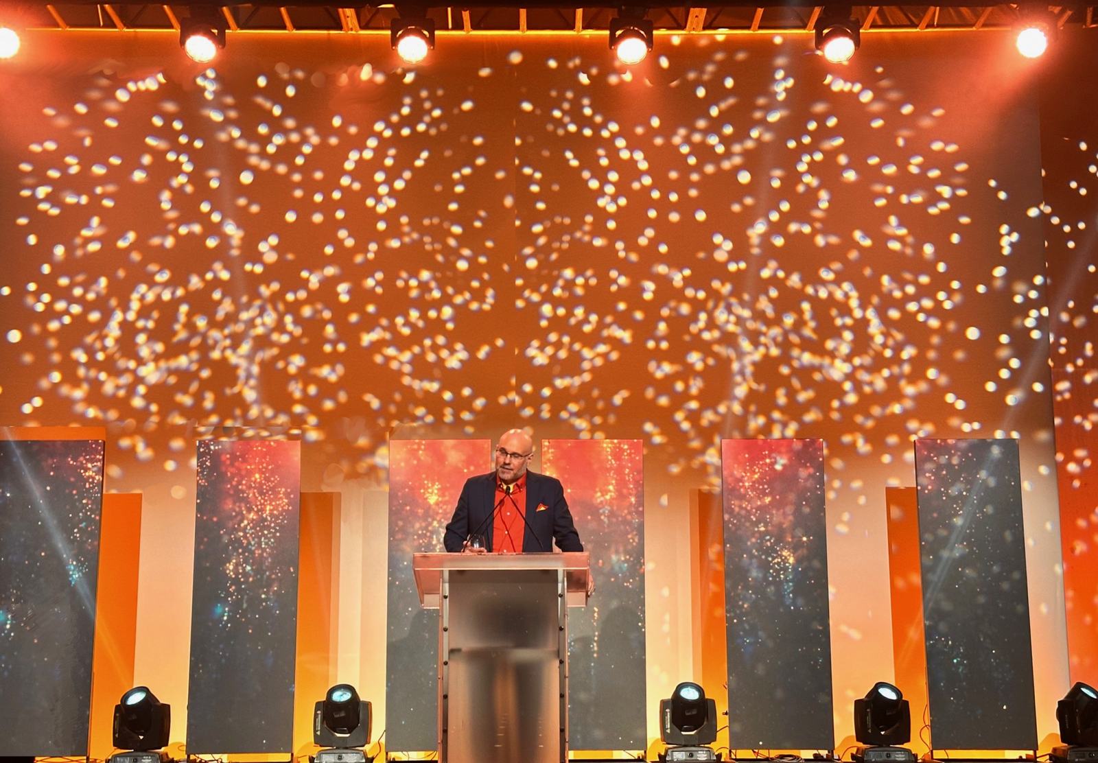Paul Tonden speaking from a lectern on a large conference stage